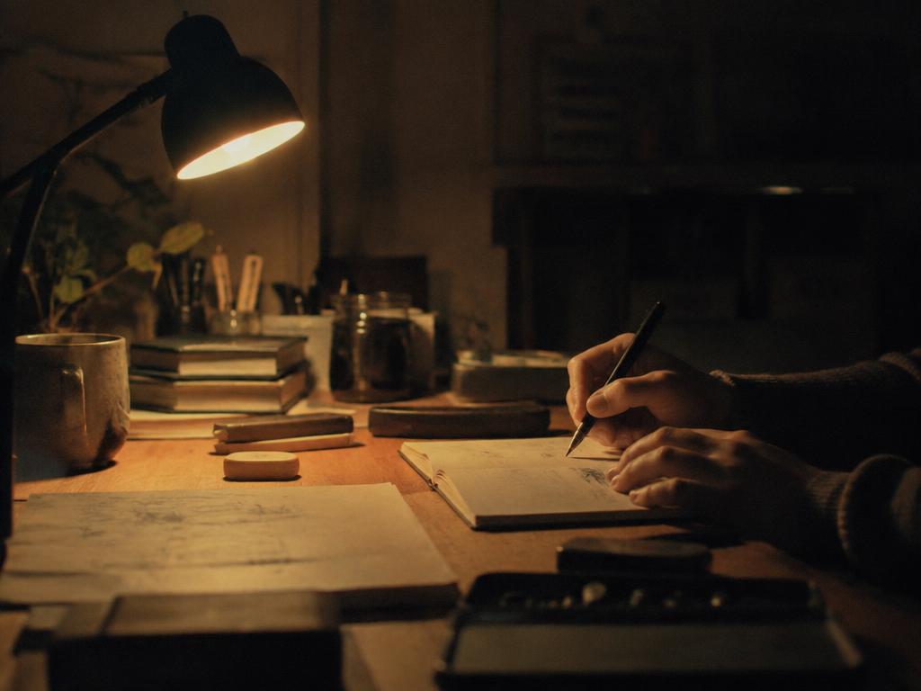 Hands working late at a desk lit by a single lamp